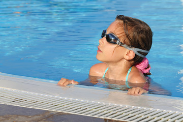 Smiling cute girl in goggles swimming in pool