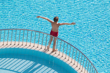 Boy sunbathing on edge of pool raised his hands up