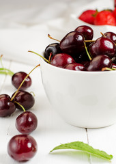 Cherries in the white bowl with strawberries in the background