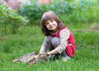 Fototapeta premium Happy little girl playing with cat on the grass