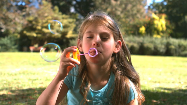Smiling young girl blowing into a bubble wand