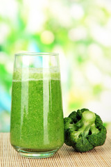 Glass of broccoli juice, on bamboo mat, on green background