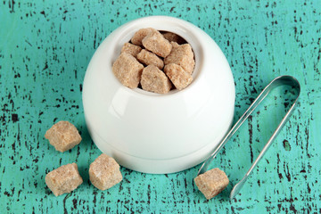 Unrefined sugar in white sugar bowl on wooden background