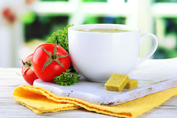 Cup of soup with bouillon cubes on wooden table