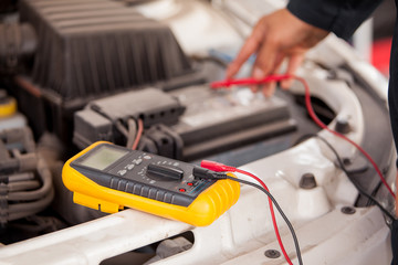 Closeup of a mechanic checking the battery of a car with a multimeter