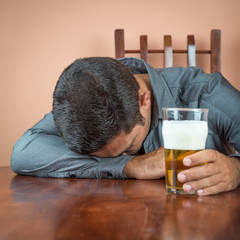 Drunk man sleeping on a table and holding a pint of beer