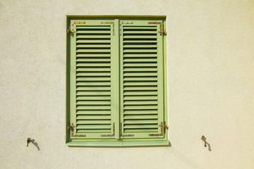 Fototapeta na wymiar Closed green shutters on a bright yellow wall.