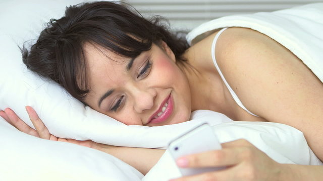 Young woman lying in bed texting