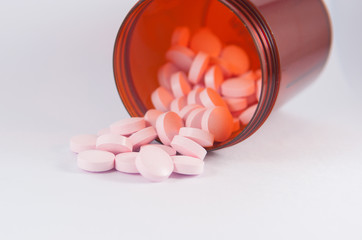 Pink tablet and brown bottle on white