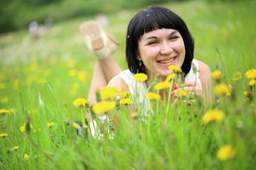 Young woman lying on grass in the field of dandelion