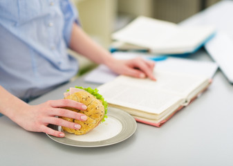 Closeup on teenage girl with sandwich and book in kitchen