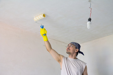 Young worker painting ceiling with roller
