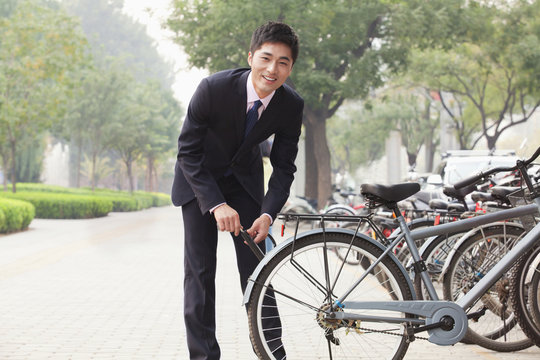 Young Businessman Locking Up His Bicycle On A City Street In Beijing