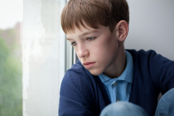 Sad teenager sitting on window