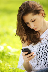 Image of young beautiful woman in summer park reading a message