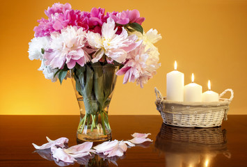Bouquet of peonies in glass vase and basket of candles