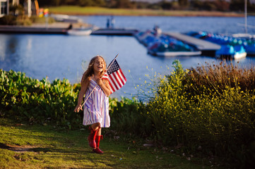 Happy adorable little girl smiling and waving American flag outs