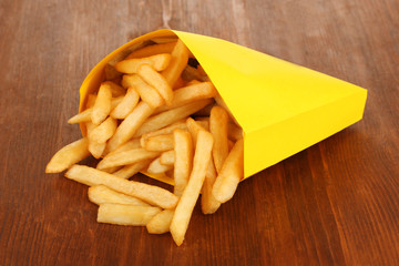 French fries in paper bag on wooden table close-up