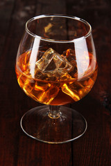 Brandy glass with ice on wooden background