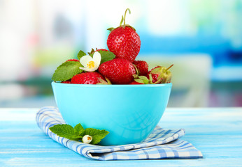 Ripe sweet strawberries in bowl on blue wooden table