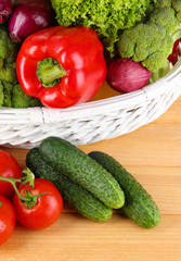 Fresh vegetables in white wicker basket on wooden background