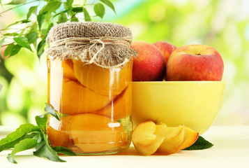 Jar of canned peaches and fresh peaches on wooden table,