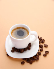 Cup of coffee with coffee beans on beige background