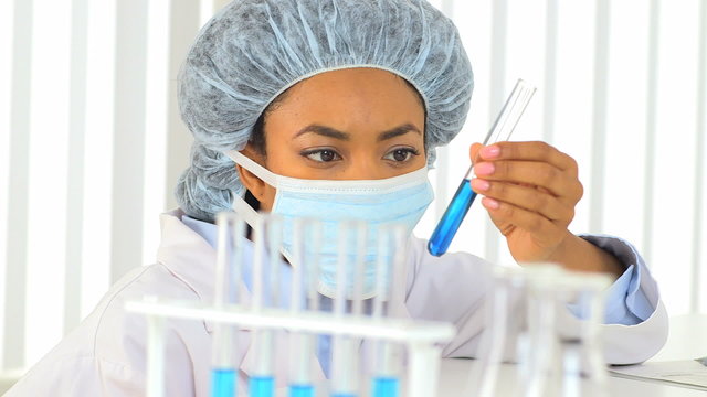 Female African American scientist analyzing blue liquid in a tes