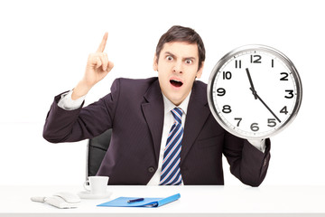 Angry man in an office, holding a clock and pointing with a fing