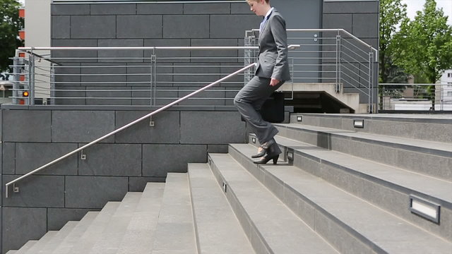 Young woman in business suit walking down staircase in slow moti