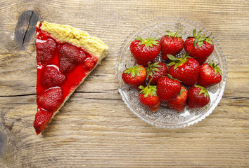 Piece of strawberry tart and fresh raw strawberries on wooden ta