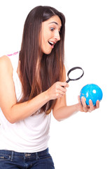 Pretty female holding a globe and using a magnifying glass while