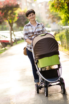 Happy young mother with baby in buggy walking