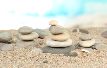 Fototapeta na wymiar Towers of sea stones on sand on bright background
