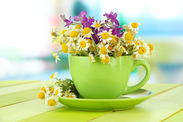 Bouquet of chamomile flowers in cup, on bright background