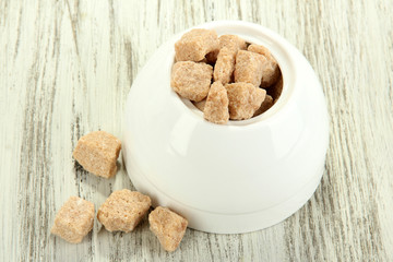 Unrefined sugar in white sugar bowl on wooden background