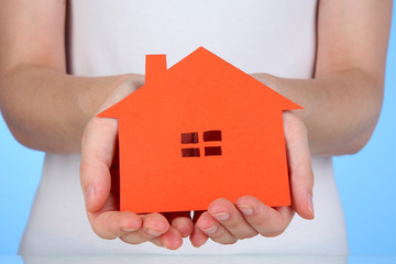 Paper house in hands on blue background