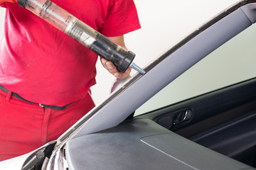 Glazier using application gun to apply adhesive for windscreen