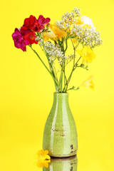 Beautiful bouquet of freesia in vase on yellow background