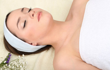 Fototapeta na wymiar Beautiful young woman lying in spa salon with flowers close up
