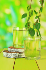 Glasses of birch sap on wooden table, on green background