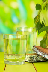 Glasses of birch sap on wooden table, on green background