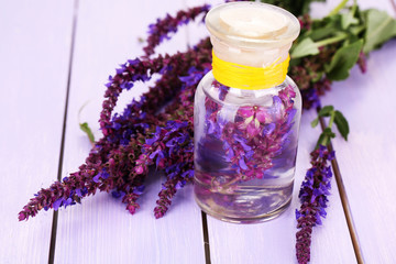 Medicine bottle with salvia flowers on purple wooden background