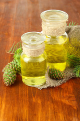 Bottles of fir tree oil and green cones on wooden background