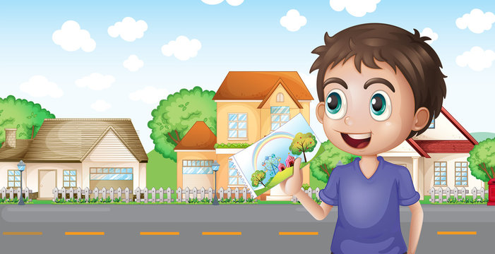 A boy holding a picture in front of the houses near the road