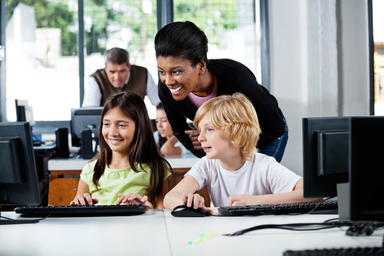 Happy Teacher Assisting Schoolchildren In Using Computer