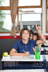 Happy Schoolboy Raising Hand In Classroom