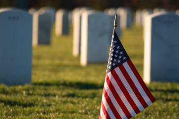 American flag in foreground of cemetery grave marker tombstones