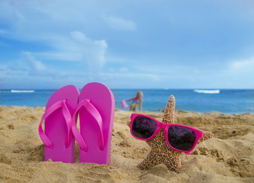 Girl's Flip flops and starfish with sunglasses on sandy beach
