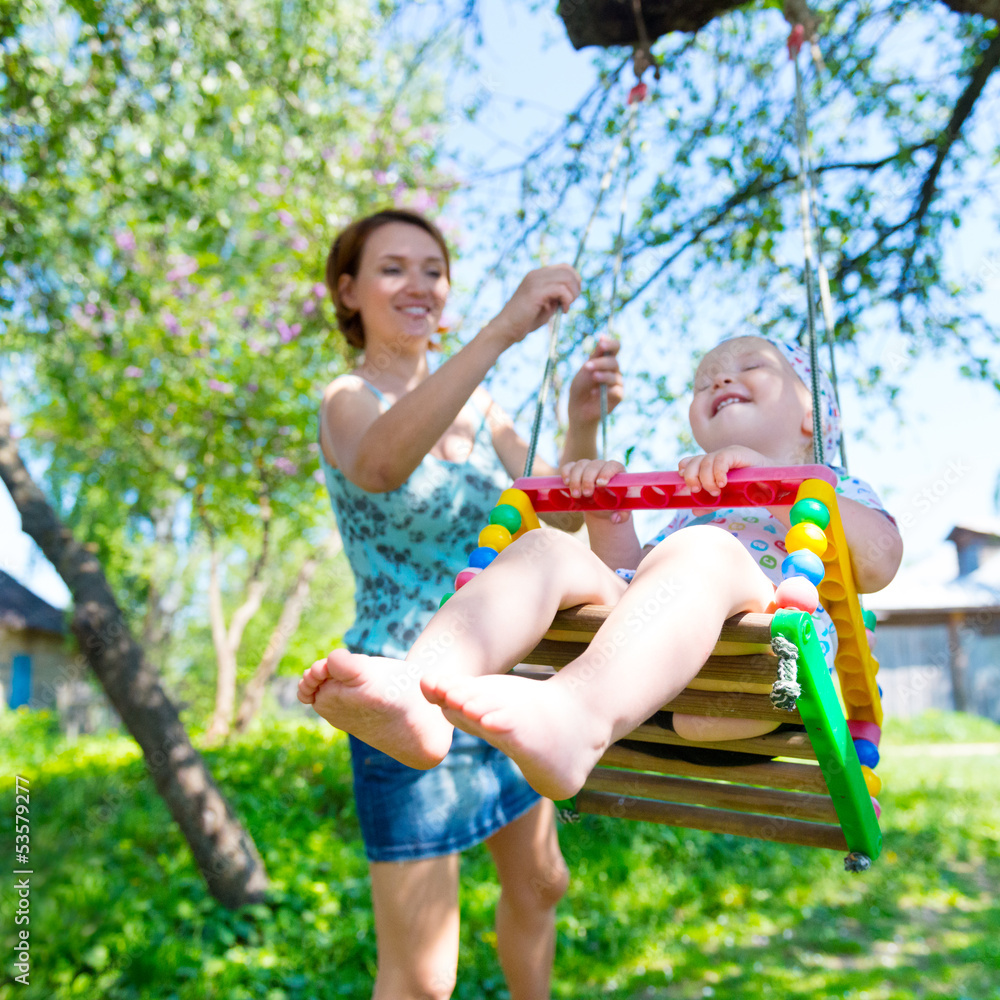 Wall mural happy mother rocking a laughing baby on a swing